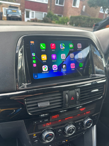 Mazda CX5 2012–2015 touchscreen displaying Apple CarPlay apps in a glossy dashboard surround.